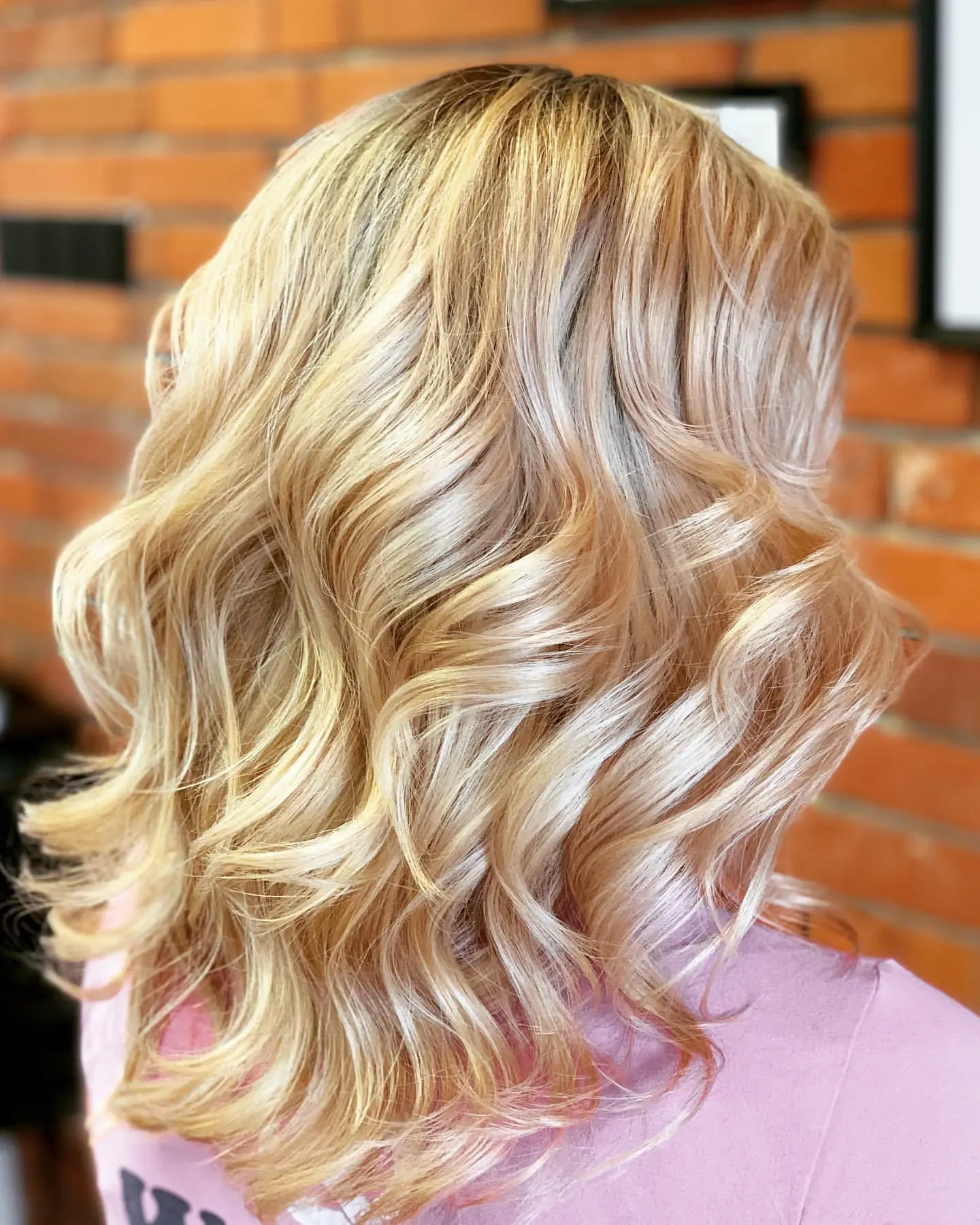 Blond fale po koloryzacji, widok od tyłu na tle ceglanej ściany salonu